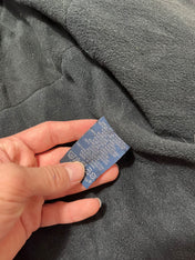 Fekete streetwear pulóver ruhacímkéje közelről, kézben tartva, összetétel és kezelési útmutató látható